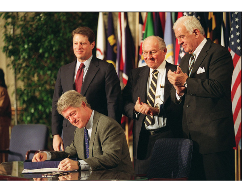 A group of men standing around a man signing a document - TN Visa Expert