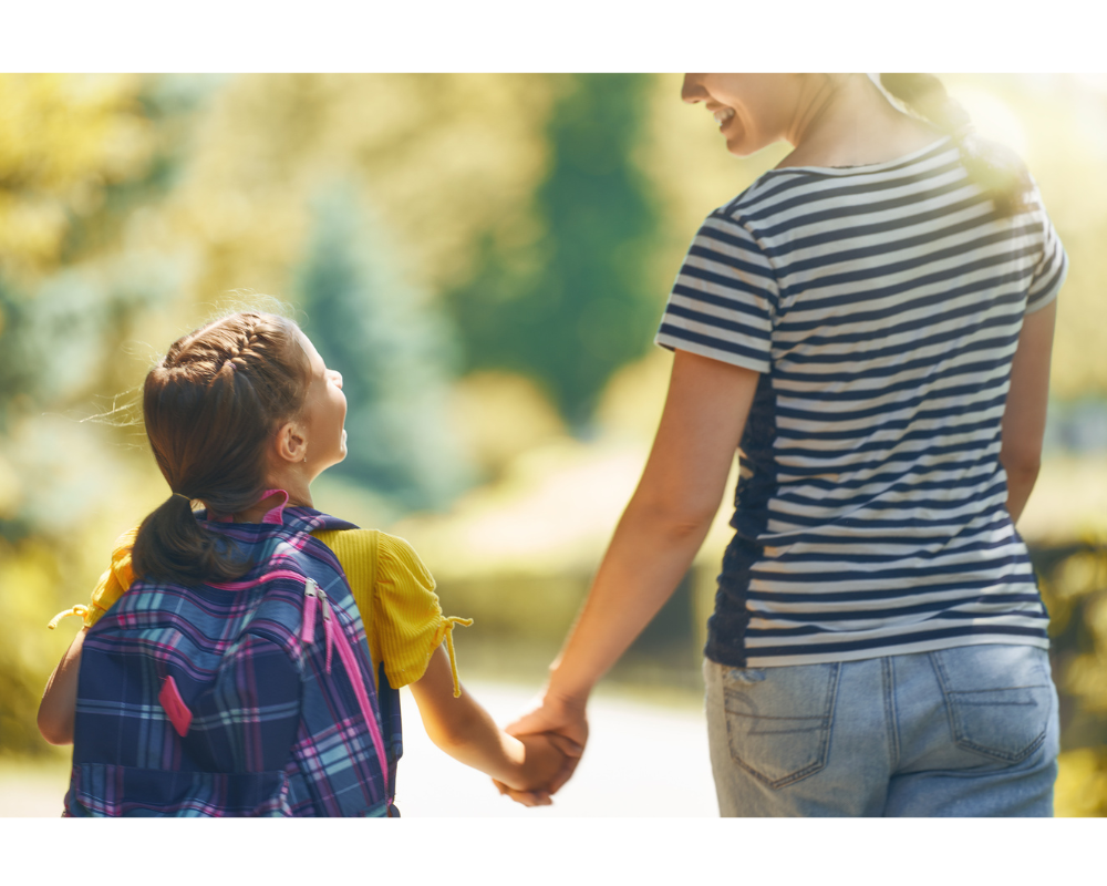 Madre e hija con mochila escolar tomadas de la mano caminando al aire libre